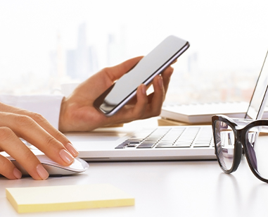 Hand holding phone and typing on computer